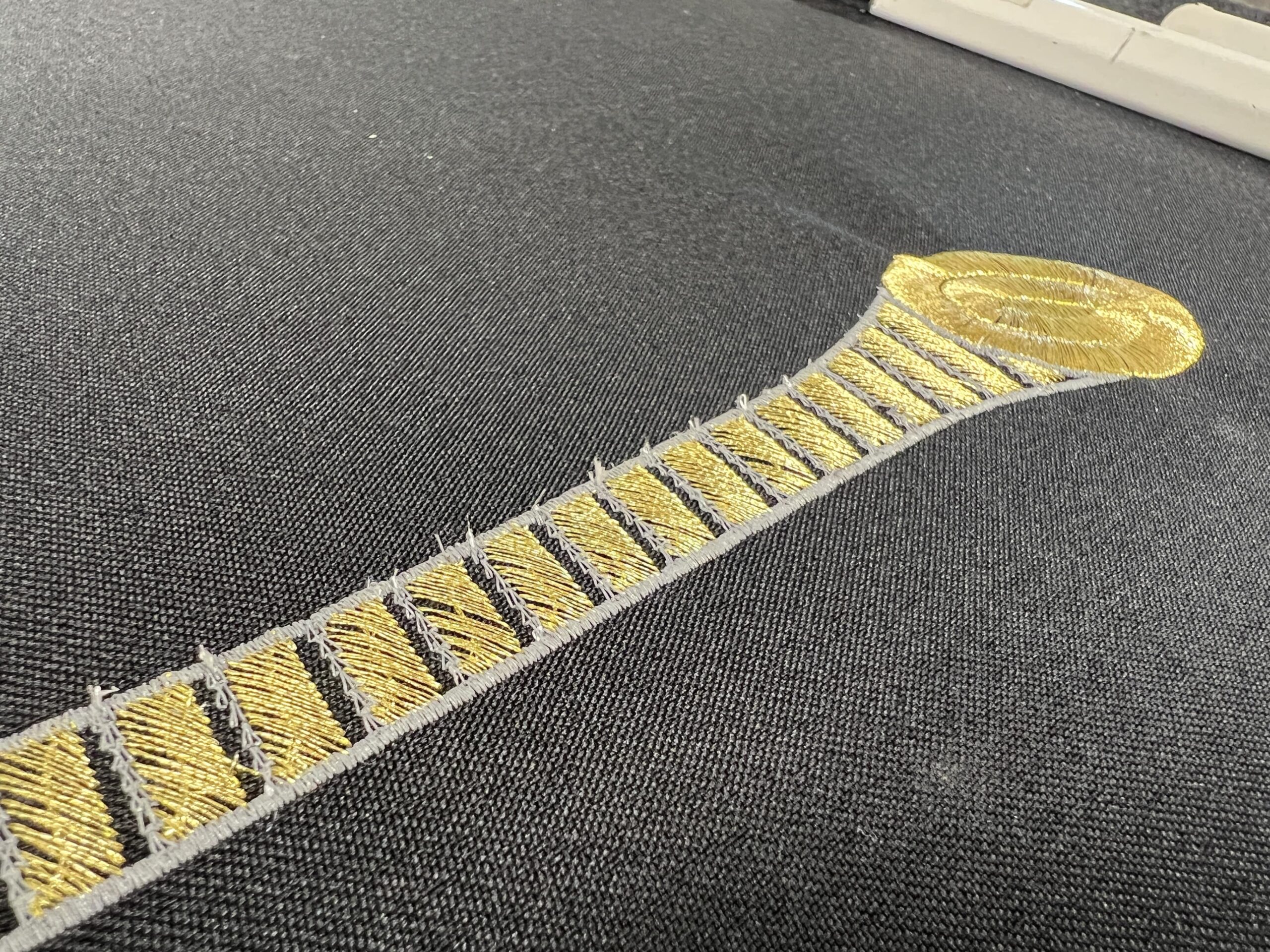 Yellow zipper motif embroidered onto black textile.