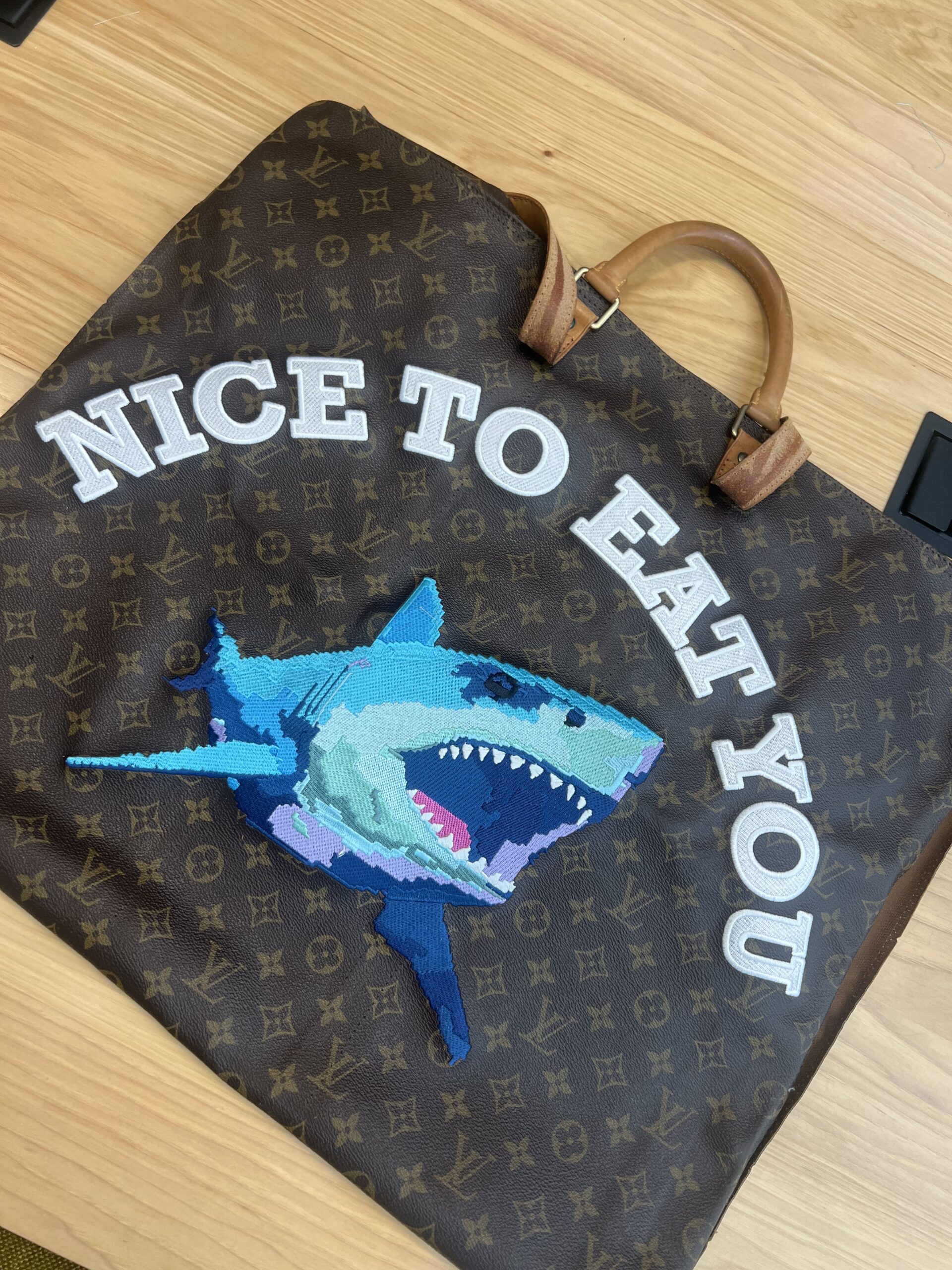Cartoonish blue shark embroidered on a bag with the text “Nice to Eat You.”