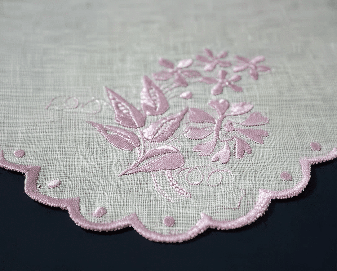 Pale pink floral embroidery with a scalloped border on white linen.