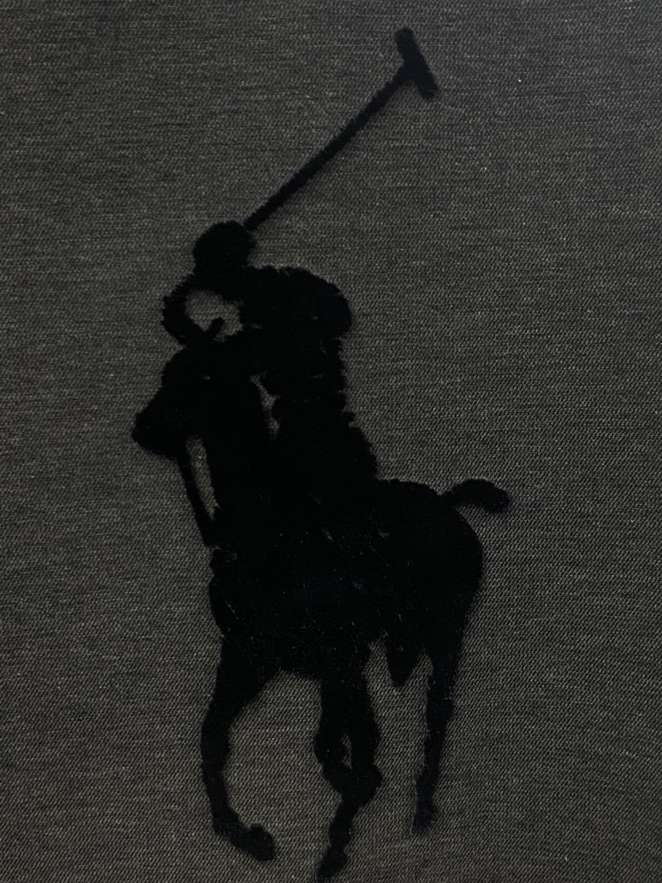 Black-on-black textured polo player silhouette on knit fabric.