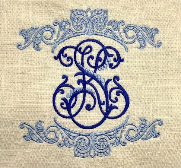 Blue monogram “SB” embroidered on beige fabric with decorative swirls.