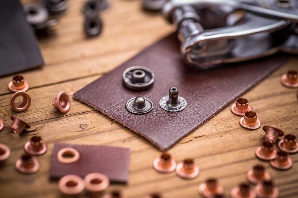 Leatherwork tools and eyelets arranged on a wood table.