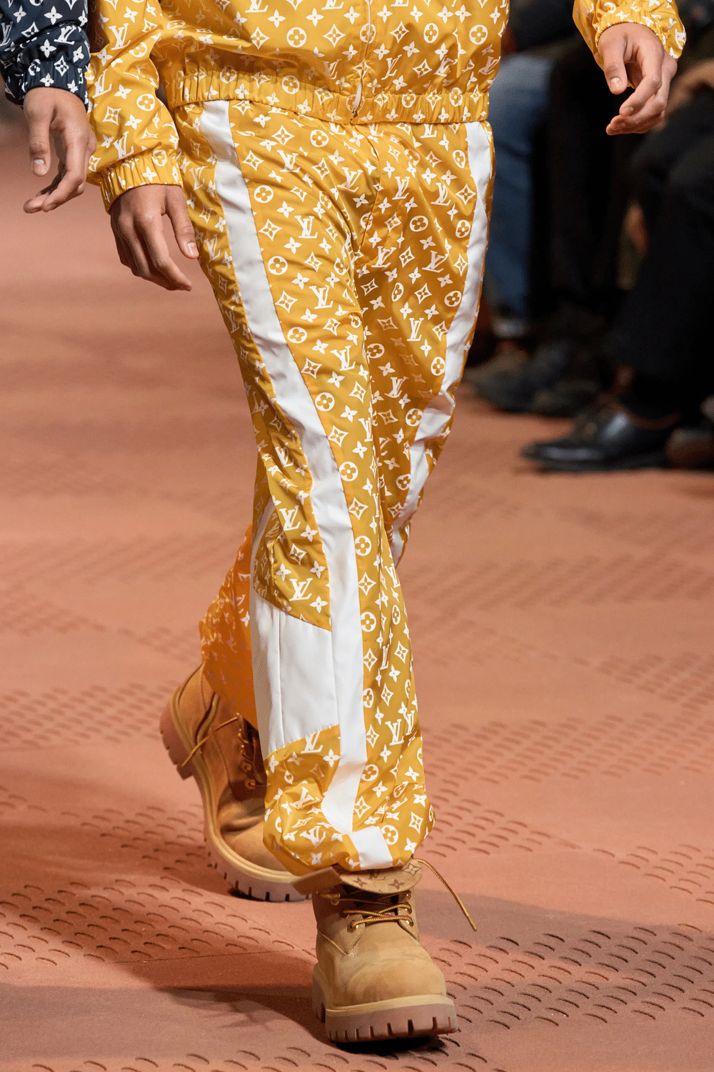 Close-up of yellow Louis Vuitton monogram track pants with white side panels, worn with tan boots.