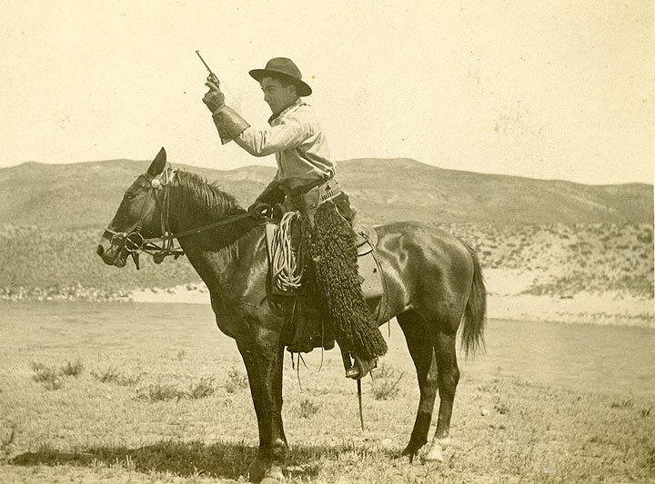Sepia-toned photo of a cowboy aiming a gun while riding a horse.