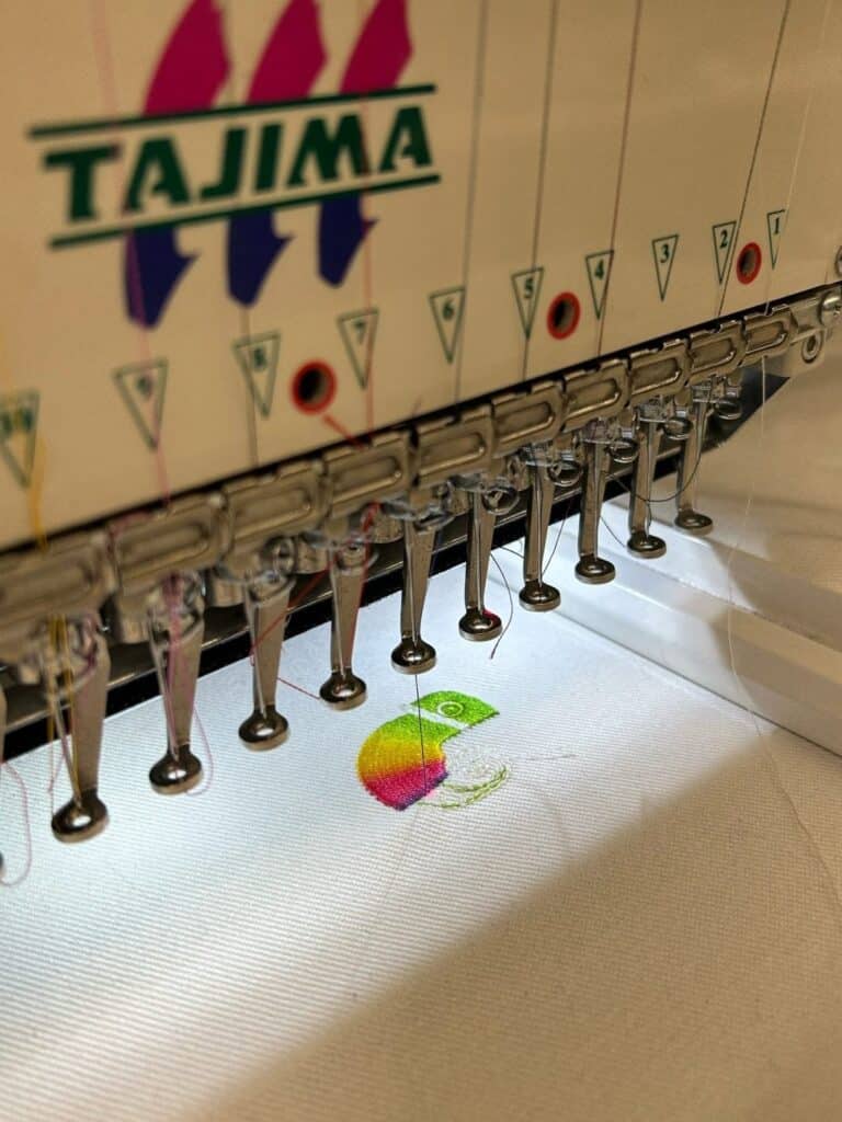 Close-up of a Tajima embroidery machine stitching a colorful circular design on white fabric.