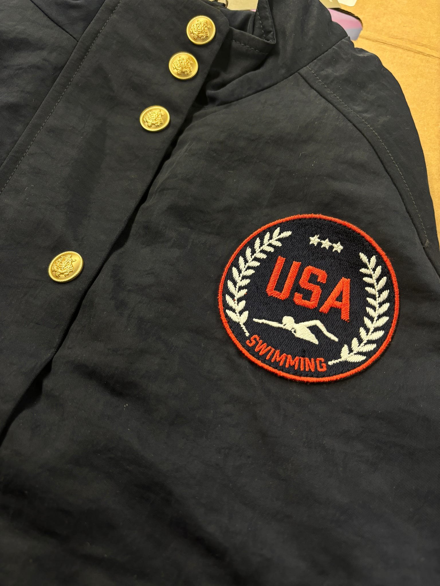 Black jacket with gold buttons and embroidered USA Swimming patch.