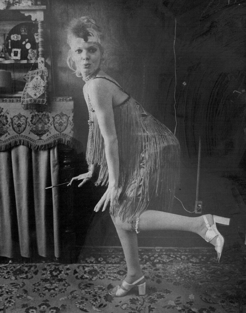 Vintage black-and-white photo of a woman in a fringed flapper dress striking a pose.