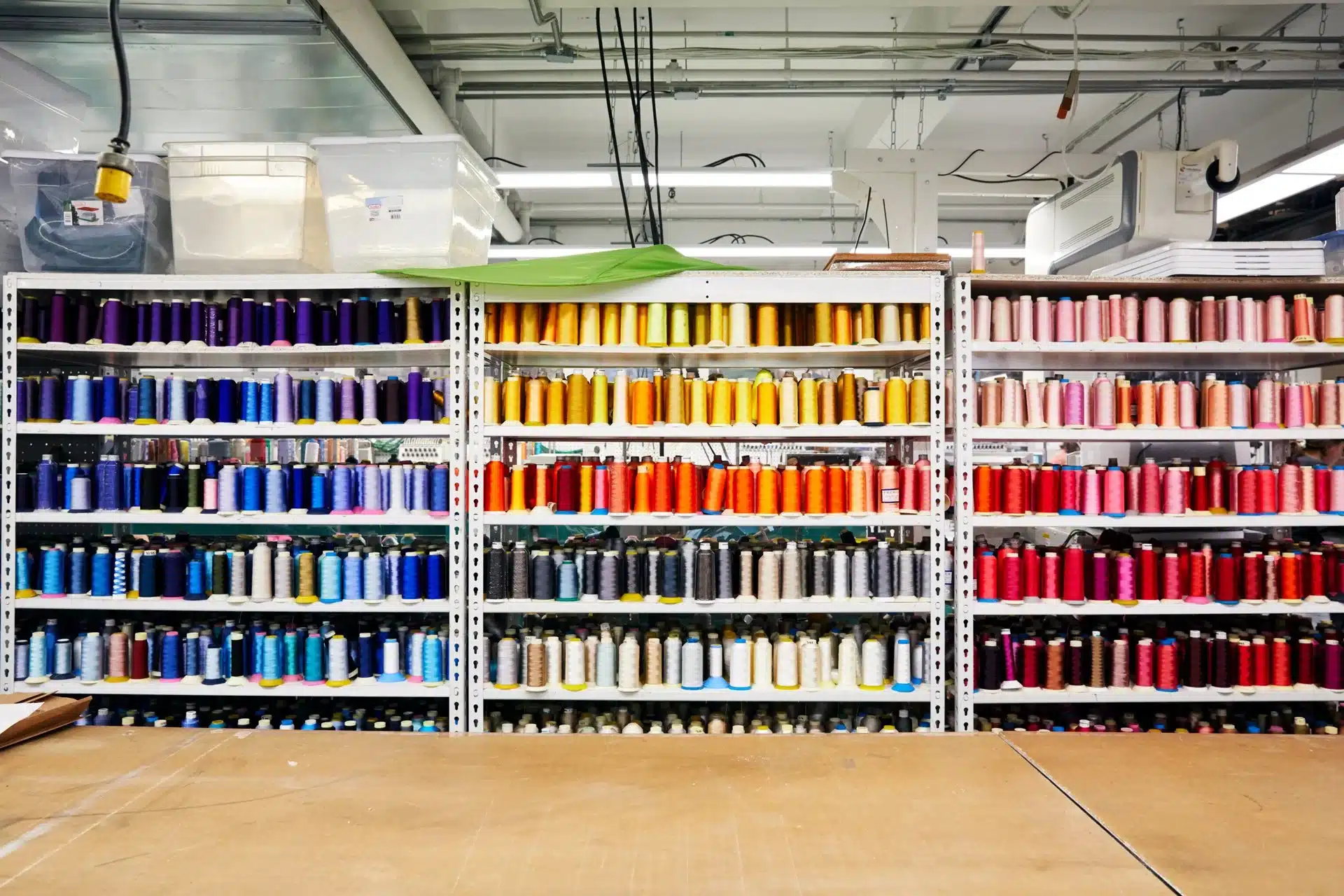 Shelves filled with neatly organized thread spools in a wide spectrum of colors, ranging from blues and purples to oranges, pinks, and reds in a textile studio