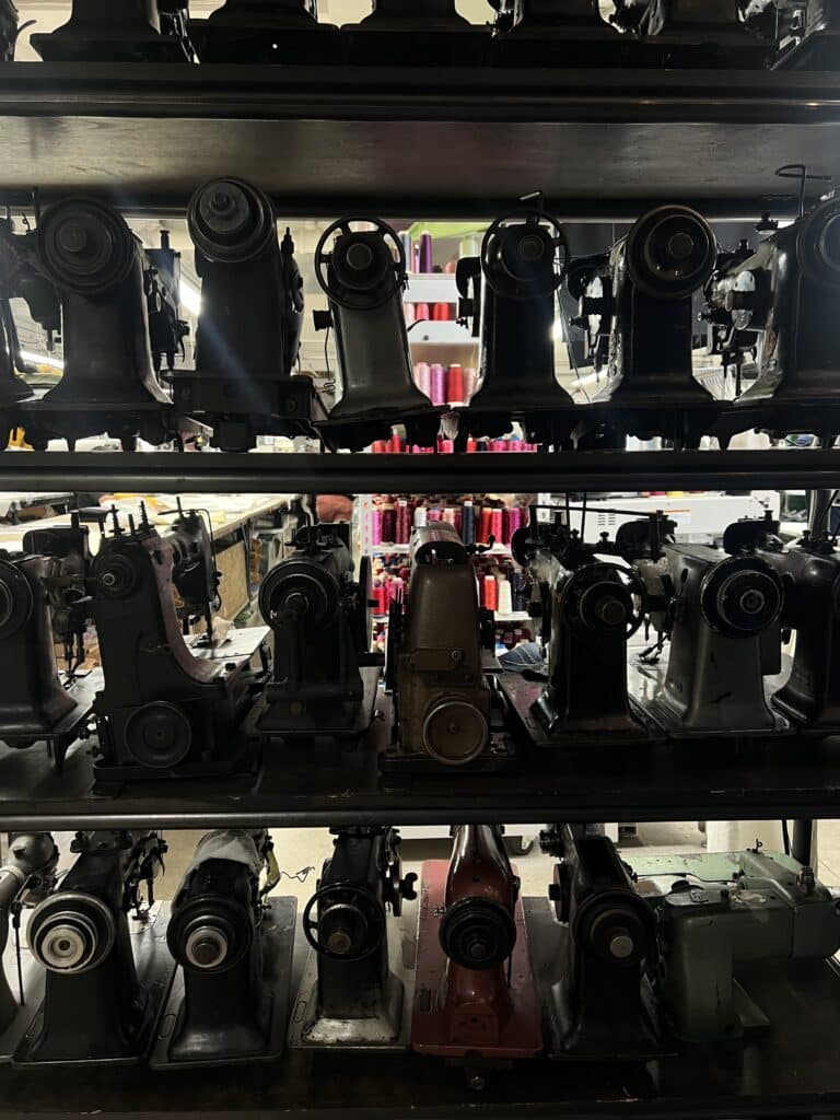 A shelf of vintage sewing machines in a dimly lit room with colorful spools of thread in the background