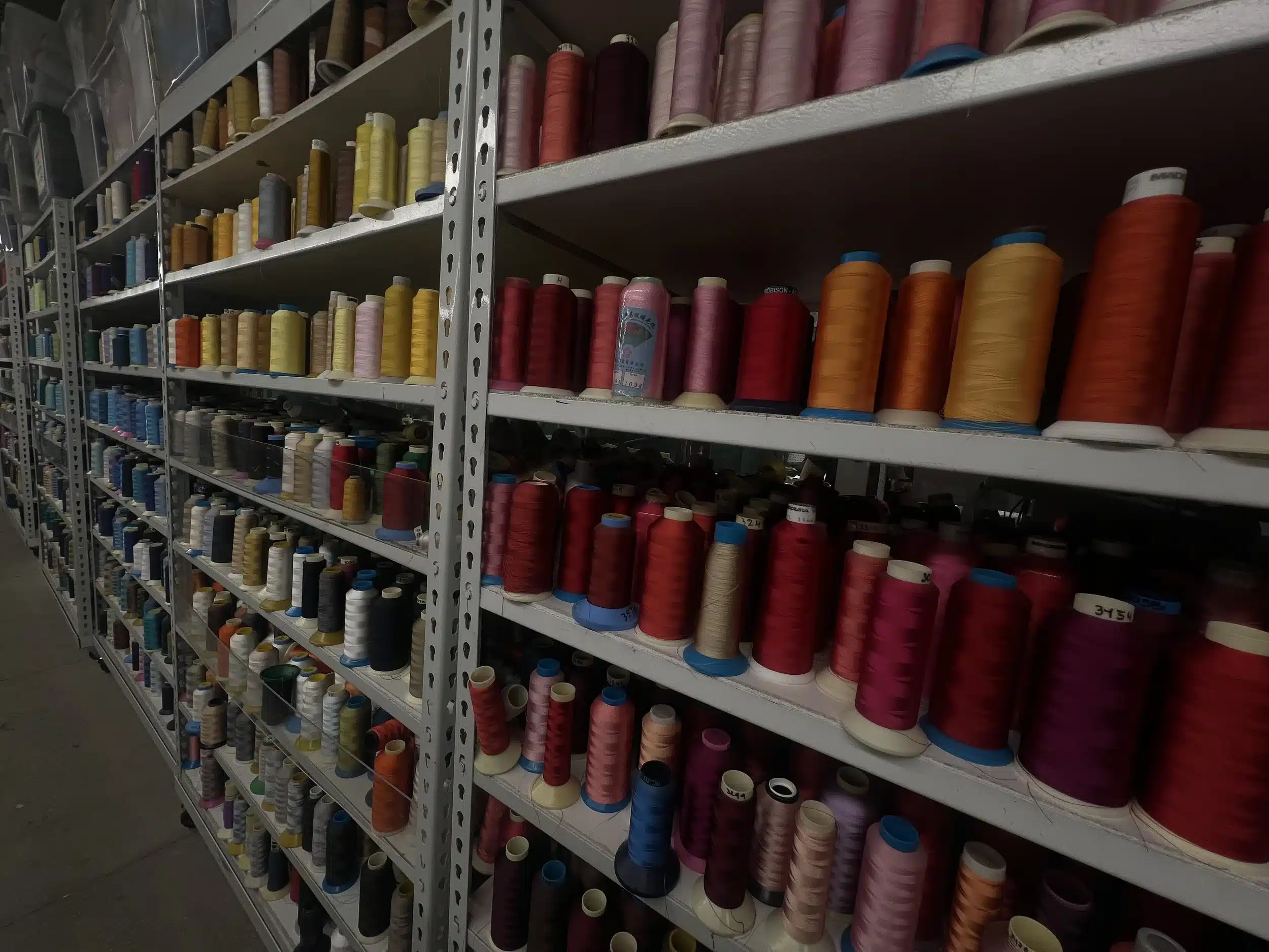 Wall-length industrial shelves stacked with colorful spools of embroidery thread in various shades