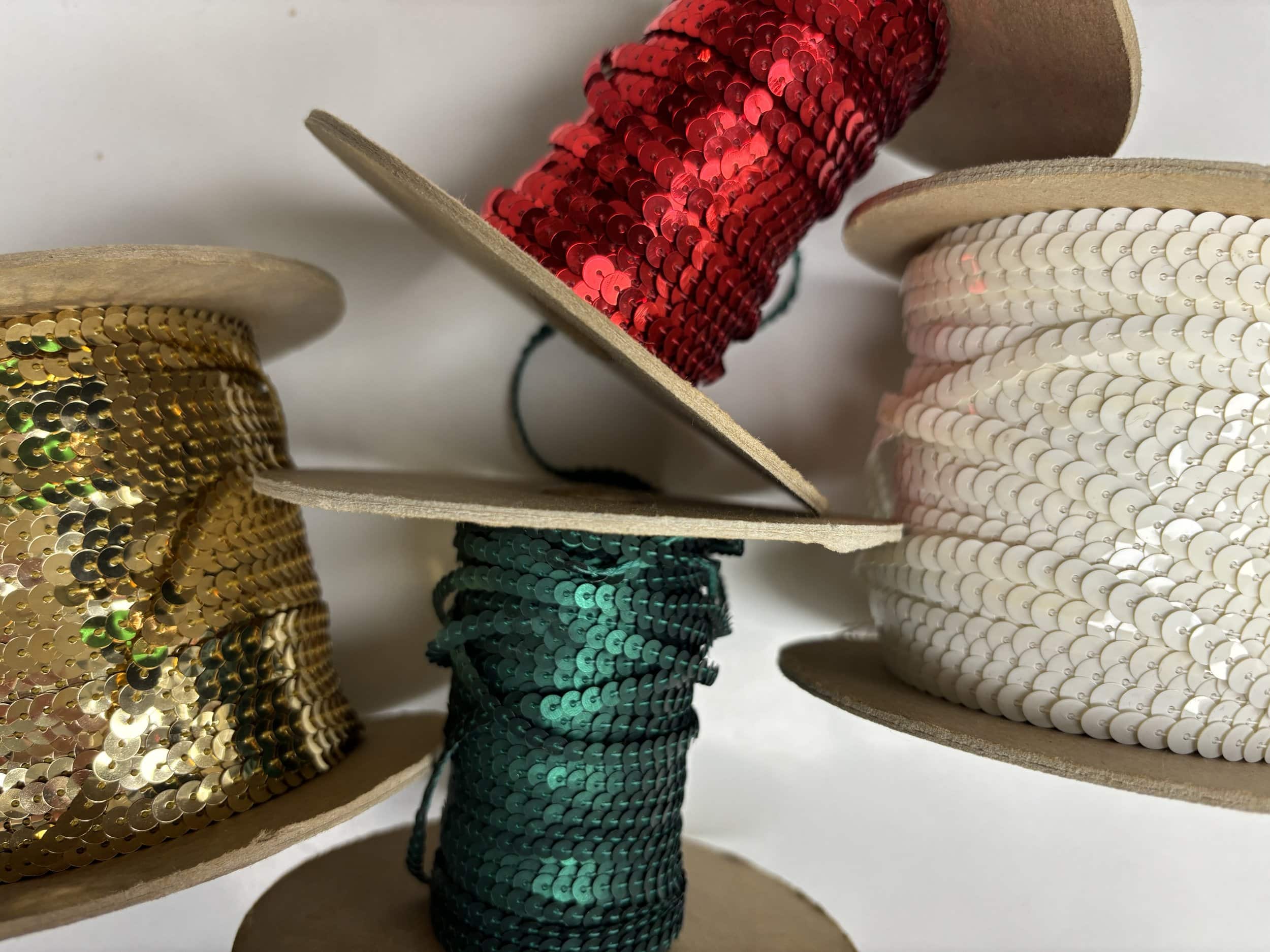 Four spools of decorative trim in gold, red, green, and white sequins and cords.