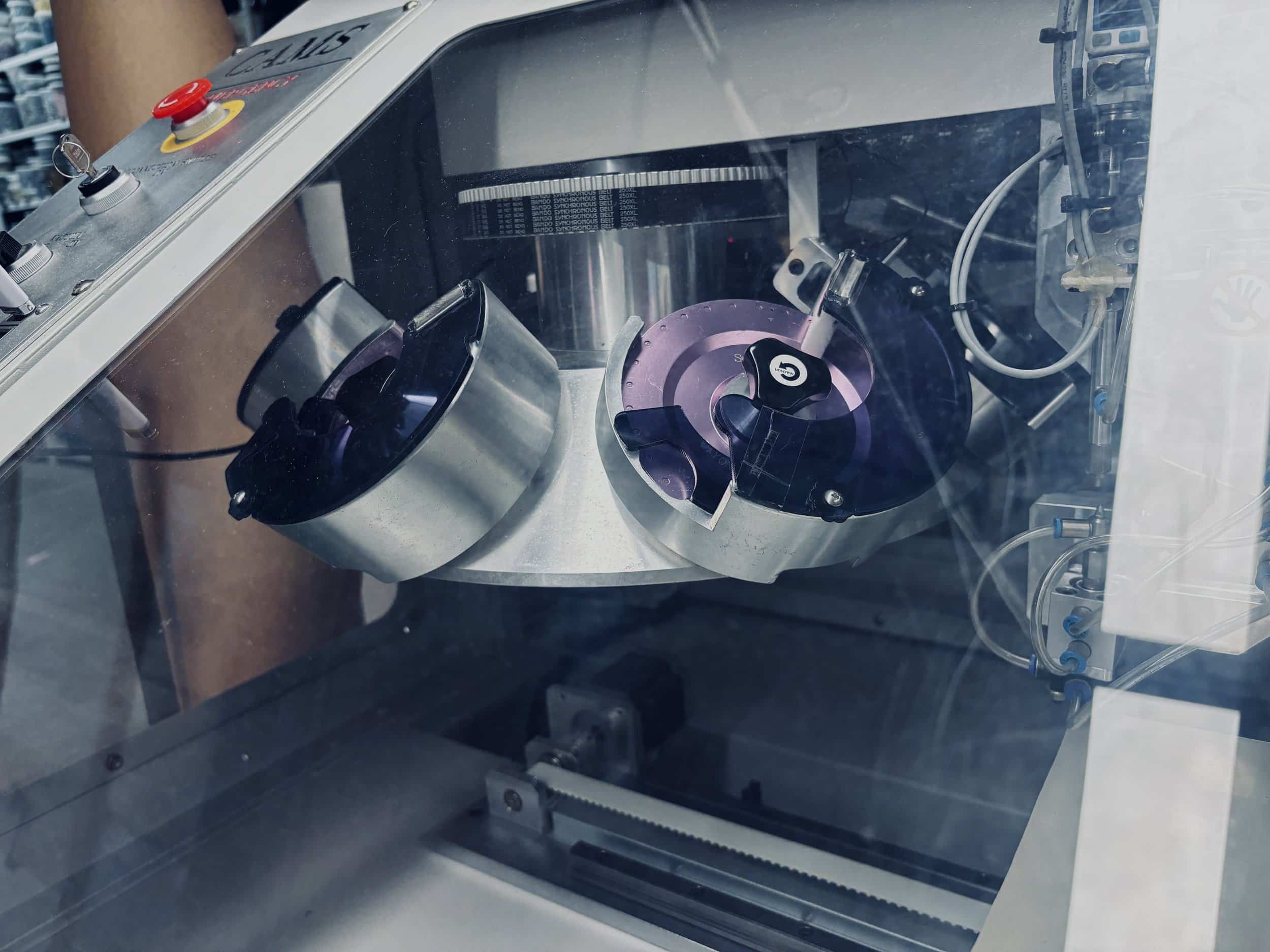 Close-up of a laser cutting machine with metallic and purple components inside a transparent protective casing.