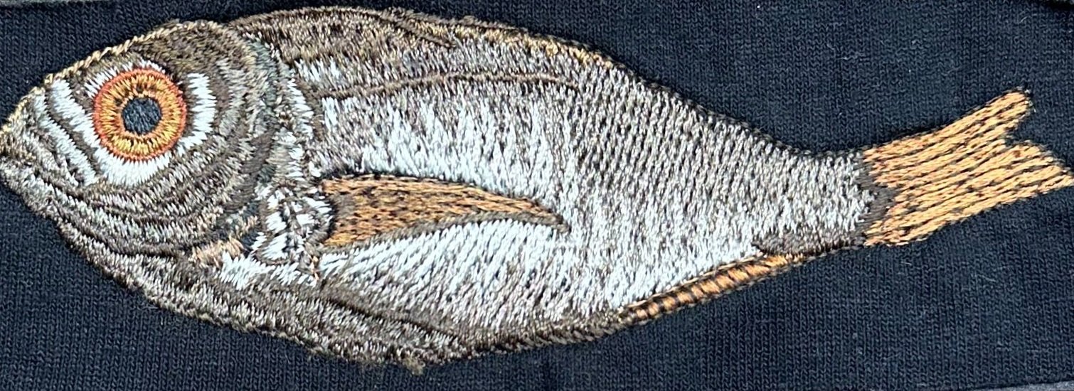 Realistic fish embroidery on dark fabric in metallic tones.