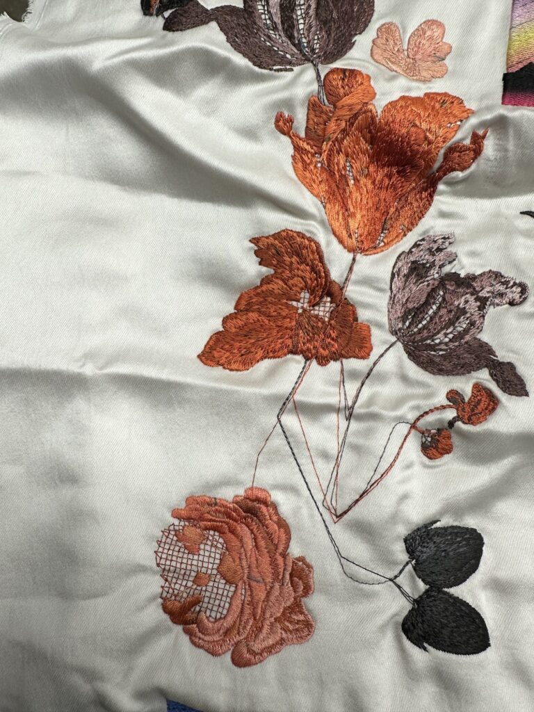 Orange and burgundy floral embroidery on ivory satin fabric.