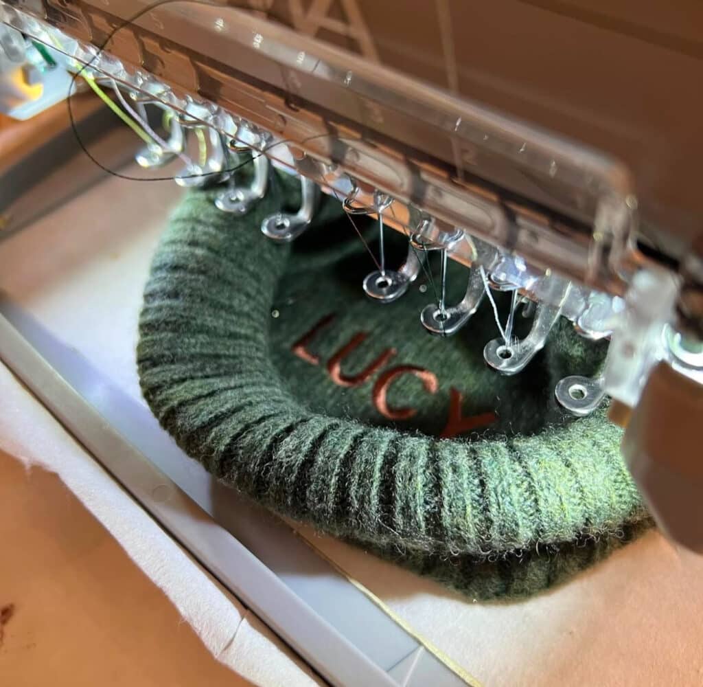 Close-up of green ribbed beanie with the name “LUCY” being machine embroidered.