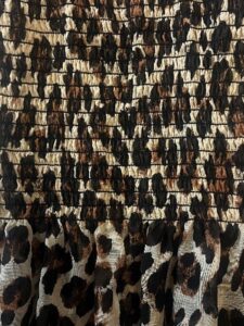Detailed image of a leopard print fabric with horizontal smocking and soft lower pleats in beige, brown, and black tones. Close-up of a ruched leopard print fabric with gathered detailing and soft pleats at the hem.
