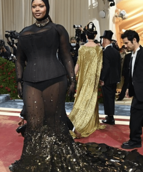 Lizzo wearing a sheer black gown with corseted bodice and dramatic black sequin train on the Met Gala red carpet.