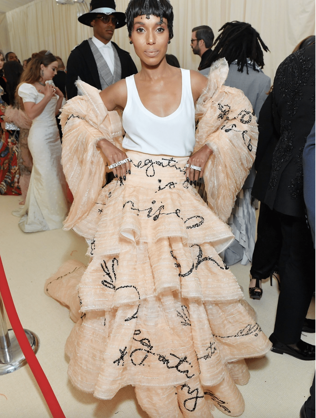 Kerry Washington wears a layered peach gown with black handwritten script and oversized matching coat at the Met Gala.