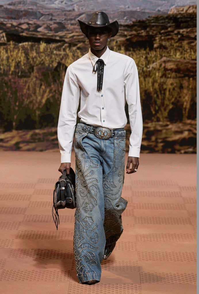 Male model in a cowboy hat wearing a white dress shirt and wide-leg paisley denim pants on the Louis Vuitton runway.