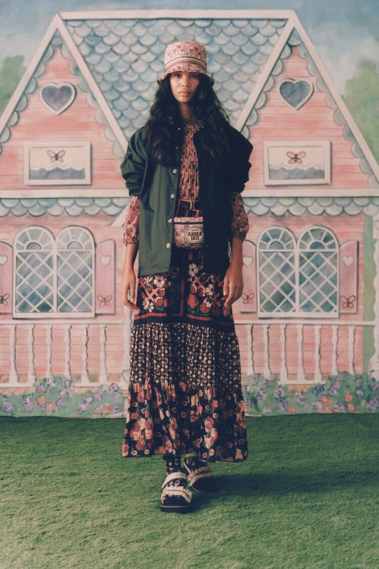 Model in a boho floral dress with a dark vest, bucket hat, and mini crossbody pouch.