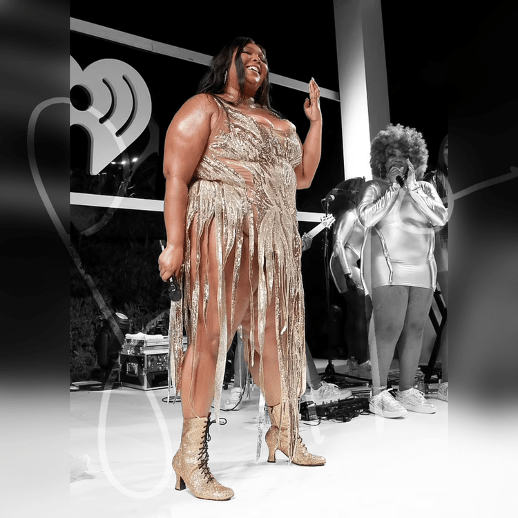 Lizzo on stage in a gold fringe dress, smiling, with microphone in hand.