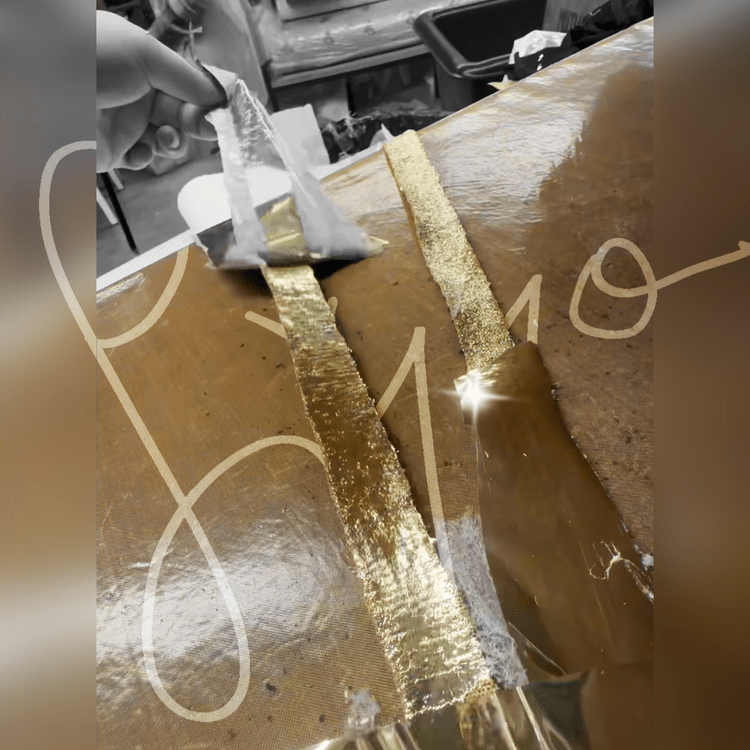 Gold foil strips being applied to a surface in a fashion studio.