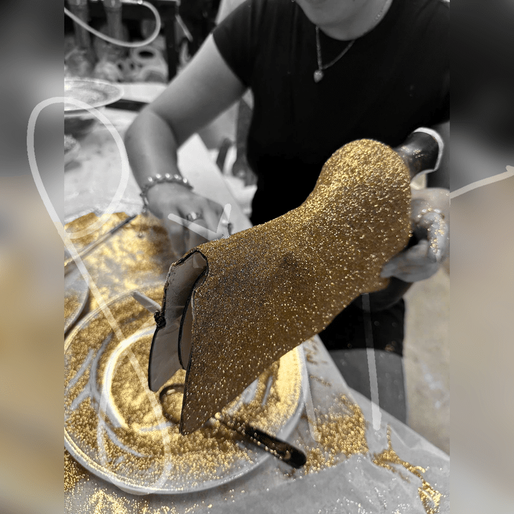 Person covering a high-heeled shoe in golden glitter.