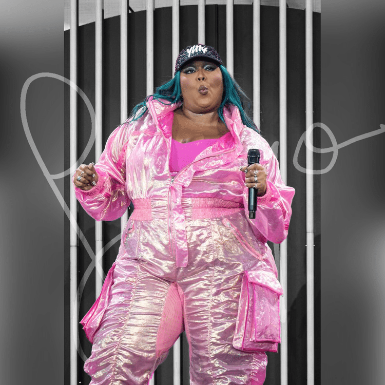 Lizzo performing on stage in a shiny pink iridescent outfit, holding a microphone.