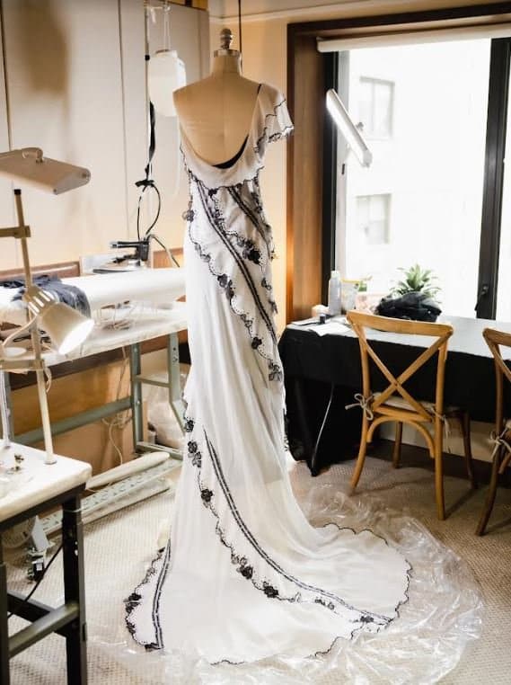 Elegant white gown with black floral trim on a mannequin in a design studio.