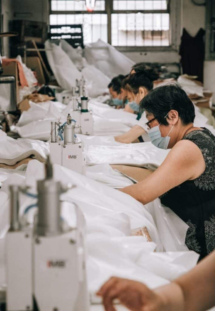 Group of workers sewing white fabric in a garment manufacturing workshop.