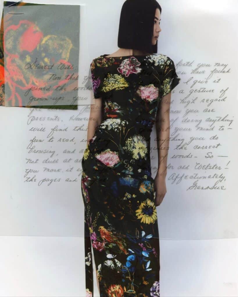 Woman wearing a black floral-print dress with colorful botanical motifs, standing in front of layered text and abstract floral imagery.