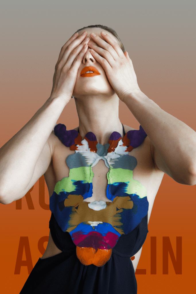 Woman in a black cut-out dress with multicolor embroidery across the chest, covering her eyes with her hands.