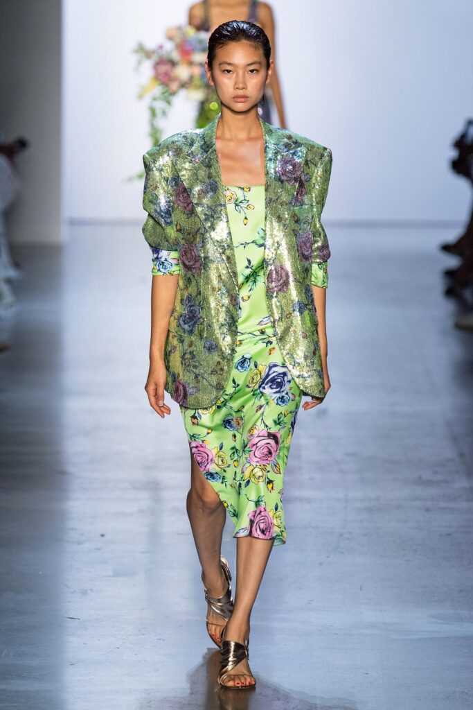 Neon suit with metallic undertones. Floral or spring-like patterns in shades of pink and blue can be seen, creating a beautiful contrast with the model’s base color.